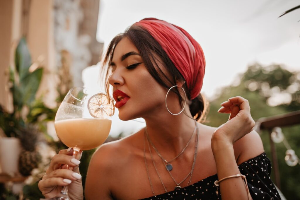 attractive brunette haired girl with pink headband round silver earrings bright bandana black shirt drinking cocktail (1)